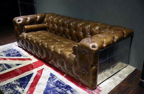 Brown tufted leather sofa with metal sides on a Union Jack rug in a vintage room.