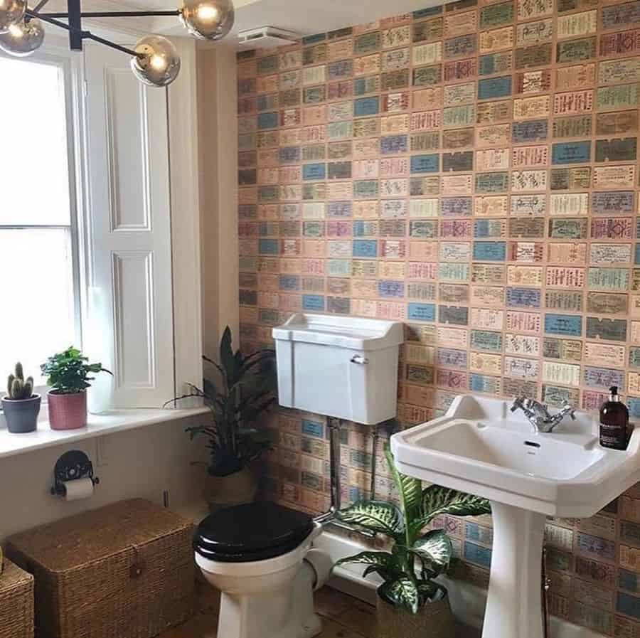 Small bathroom with ticket stub wallpaper, pedestal sink, and potted plants.