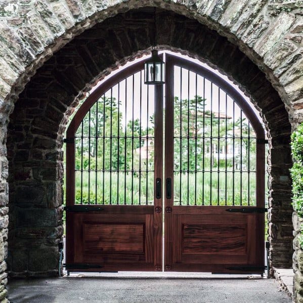 Arched wood-and-metal gate with vertical iron bars, framed by a rustic stone archway.