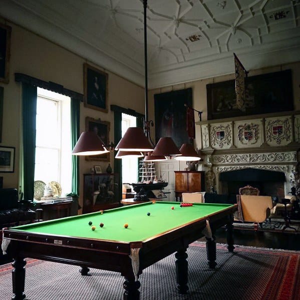 Elegant billiard room with ornate fireplace, green felt table, and vintage decor elements.