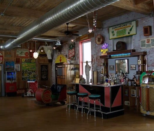 Retro-themed bar with vintage signs, stools, a jukebox, and a drink counter in a rustic setting