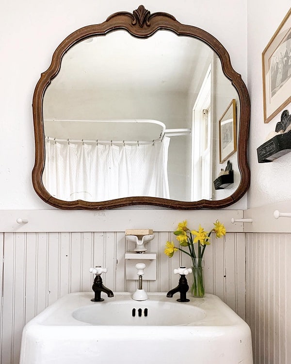 Farmhouse-style bathroom with ornate mirror, white sink, and daffodils in a vase