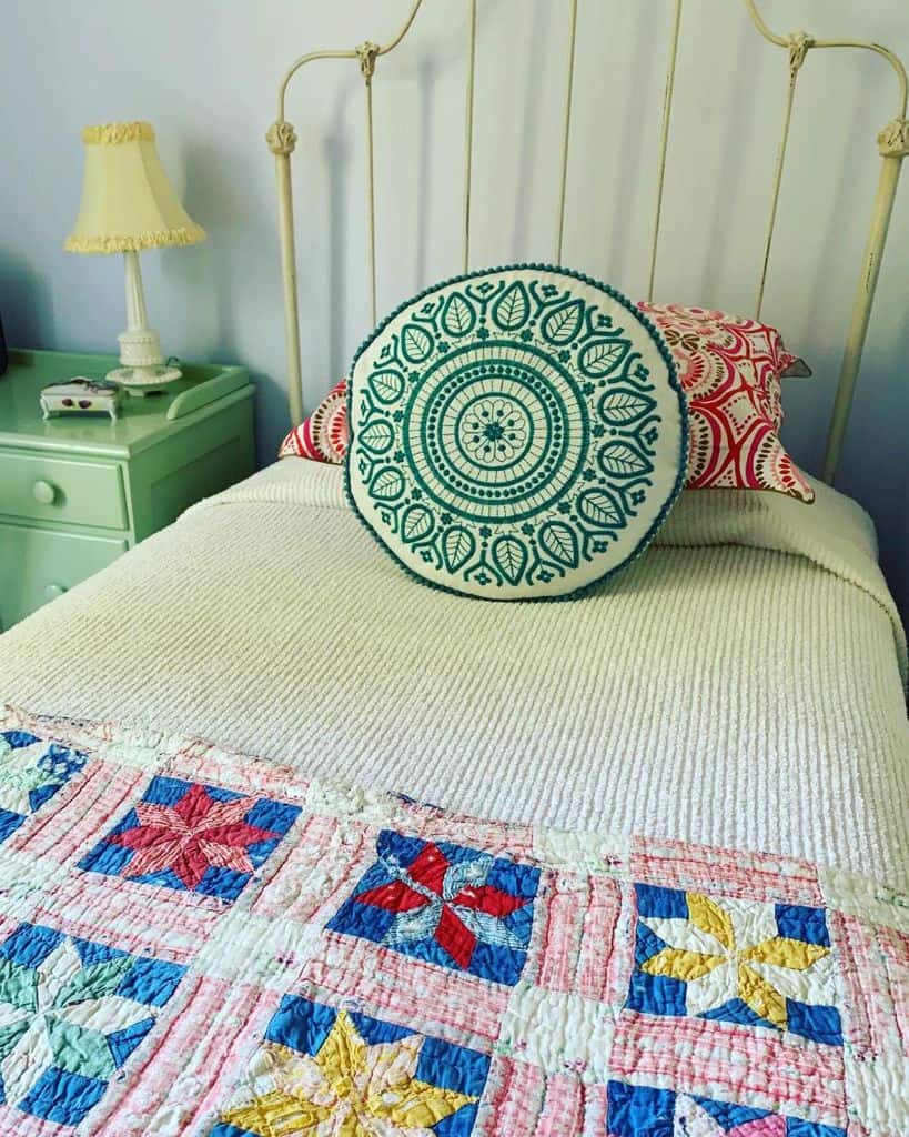 Farmhouse bedroom with an antique iron bed, colorful quilt, round decorative pillow, and green bedside table