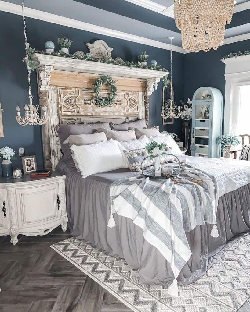 Farmhouse-style bedroom with rustic headboard, cozy linens, chandeliers, and decorative greenery accents