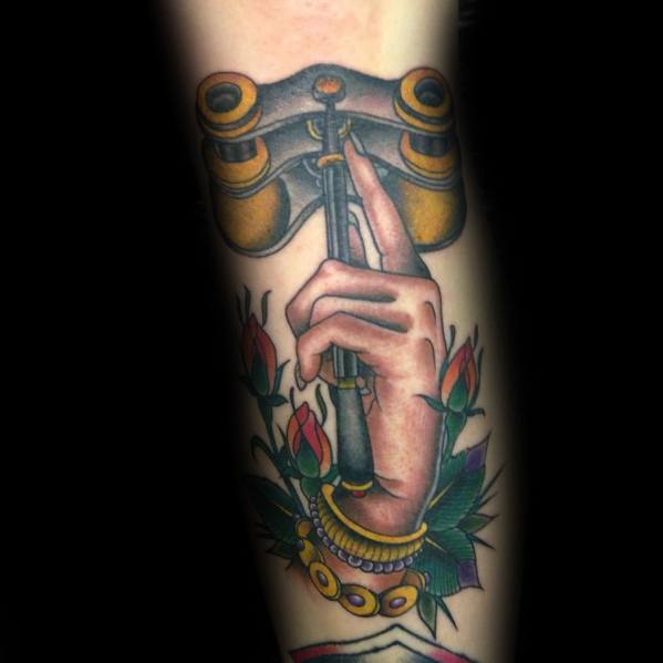 Traditional-style tattoo of a hand elegantly holding vintage opera binoculars, surrounded by roses and jewelry, symbolizing sophistication.