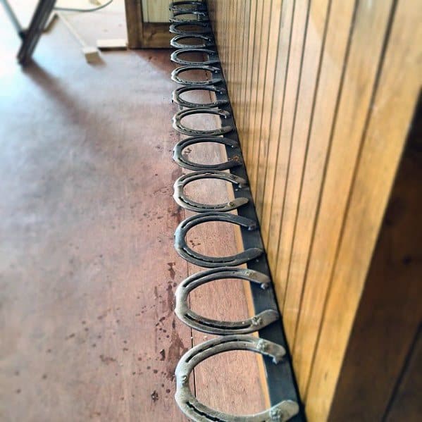 Bar foot rail made of vintage horseshoes mounted along a wooden bar with rustic wood flooring.