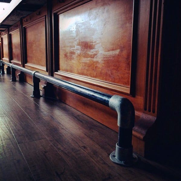 Vintage industrial-style iron pipe foot rail attached to a wooden bar with dark wood flooring.