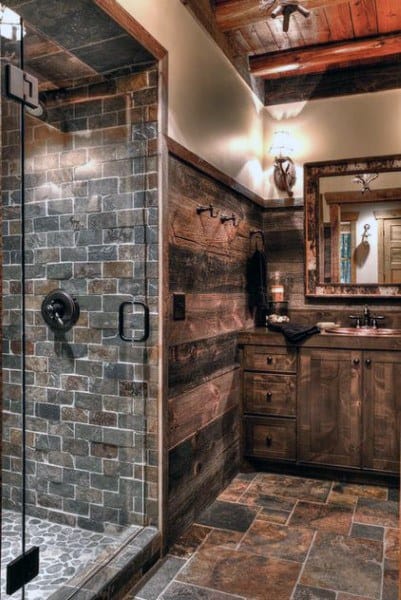 Rustic bathroom with stone tiles, wooden cabinets, and a rustic glass shower door