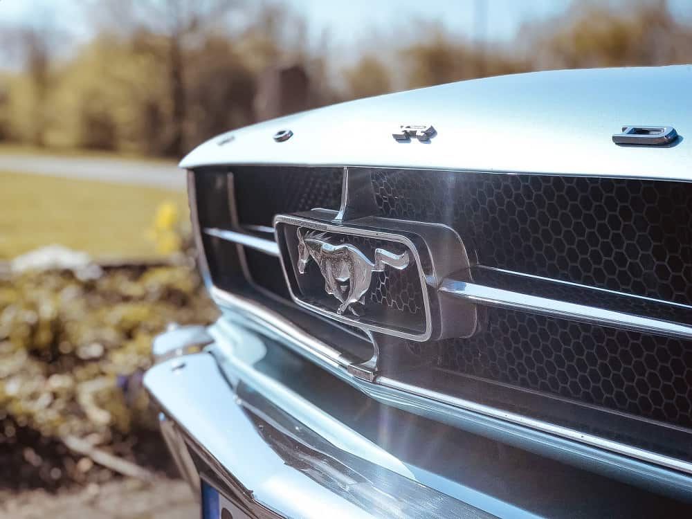 front grill of a vintage mustang, focusing on the logo, gleaming in the sunlight