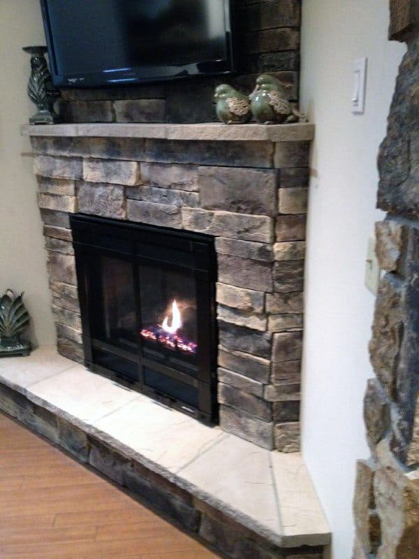 Stone corner fireplace with black insert, flat mantel decor, and mounted TV above.