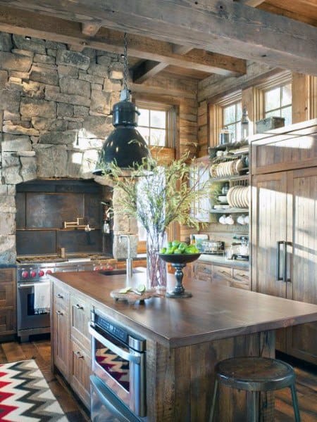 Rustic kitchen with stone walls, wood cabinets, industrial lighting, and open shelving.