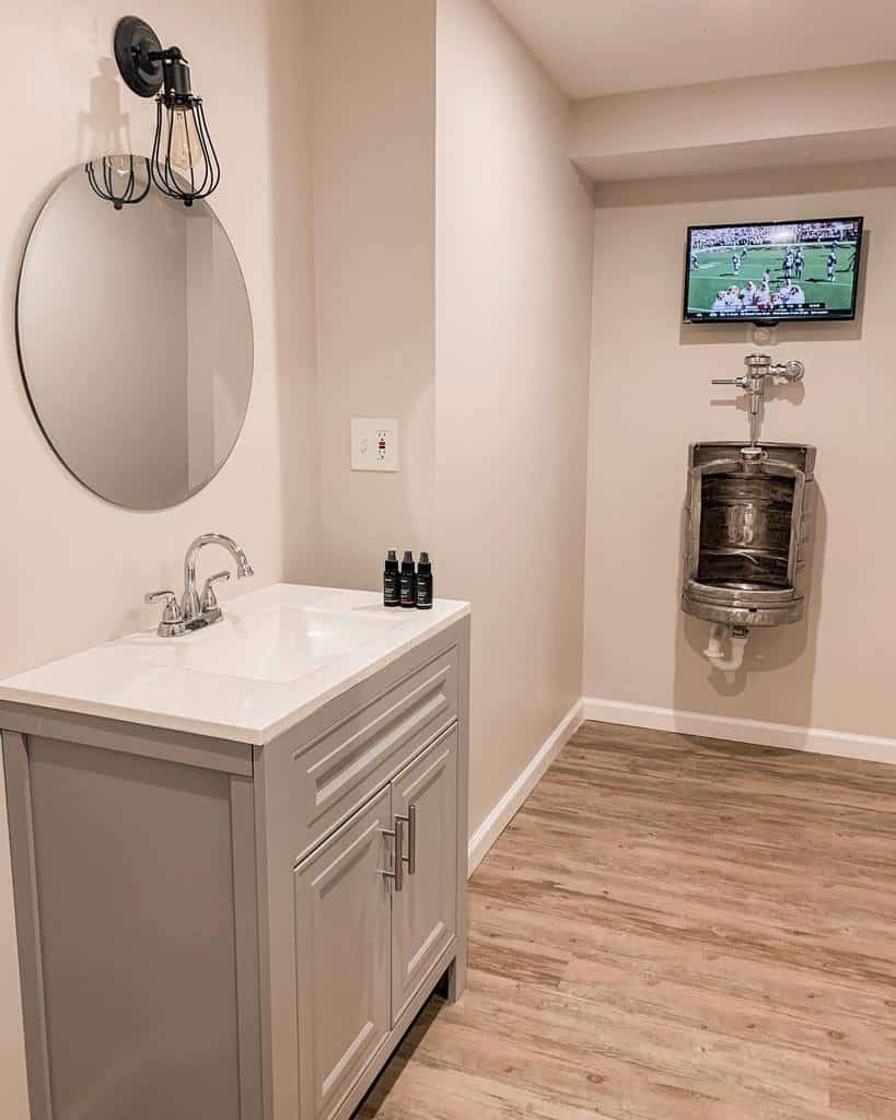 Minimalist bathroom with wooden floors, round mirror, and wall-mounted TV above urinal.
