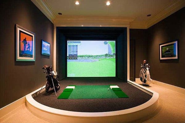 Golf simulator room with a large screen, golf clubs, and framed pictures on dark walls