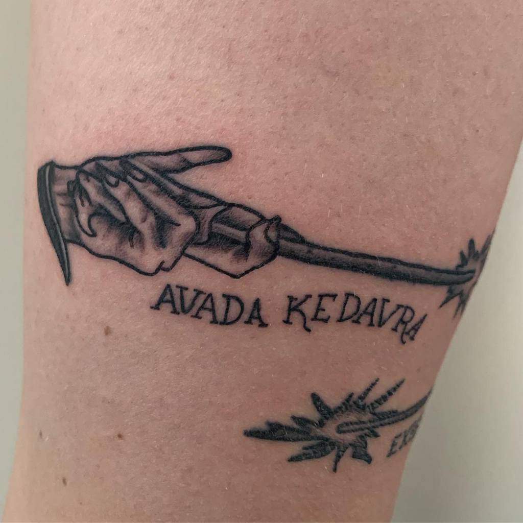Dark Harry Potter tattoo of a skeletal hand holding a wand, casting 'Avada Kedavra,' and spell effects