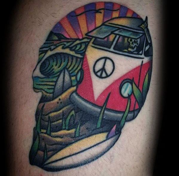 Colorful tattoo of a Volkswagen van with a skeleton driver, set in a psychedelic landscape with waves, desert, and sunset inside a skull shape.