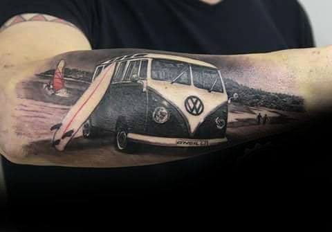 Realistic tattoo of a black and white Volkswagen van parked at the beach with a surfboard leaning on it and surfers in the background.