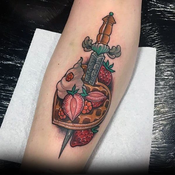 Traditional-style tattoo featuring a heart-shaped waffle with strawberries, whipped cream, and a dagger piercing through, blending sweetness with bold symbolism.