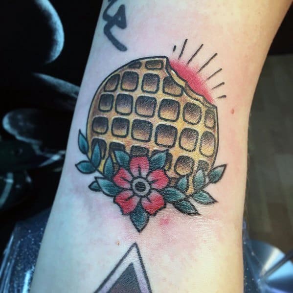 Traditional-style waffle tattoo with a bitten edge, floral accents, and bold shading, blending classic tattoo aesthetics with a fun breakfast theme.
