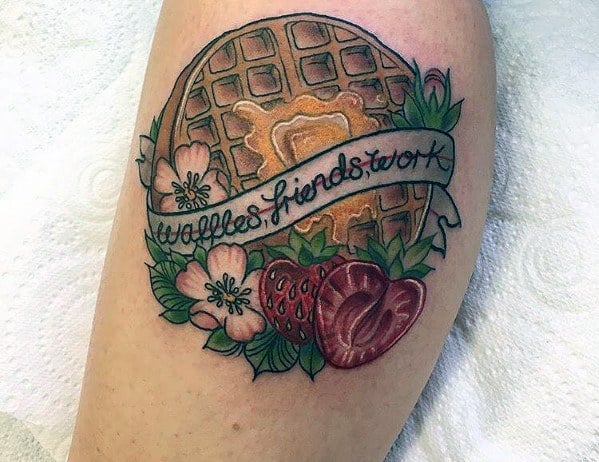 Traditional-style waffle tattoo with melted butter, a banner reading "waffles, friends, work," floral accents, and strawberries, blending food and friendship themes.
