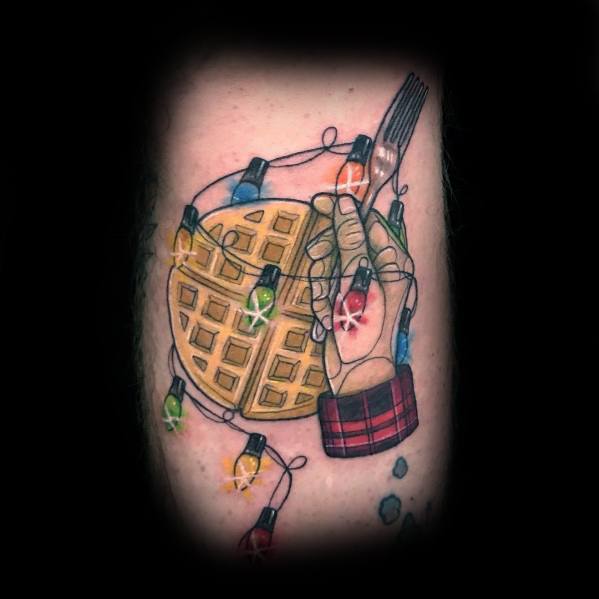 Detailed waffle tattoo featuring a hand holding a fork, wrapped in glowing Christmas lights, blending festive and rustic elements with a breakfast theme.