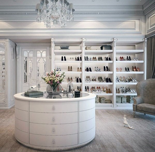 Elegant walk-in closet with white crown molding, crystal chandelier, and stylish shoe shelves, creating a luxurious storage space