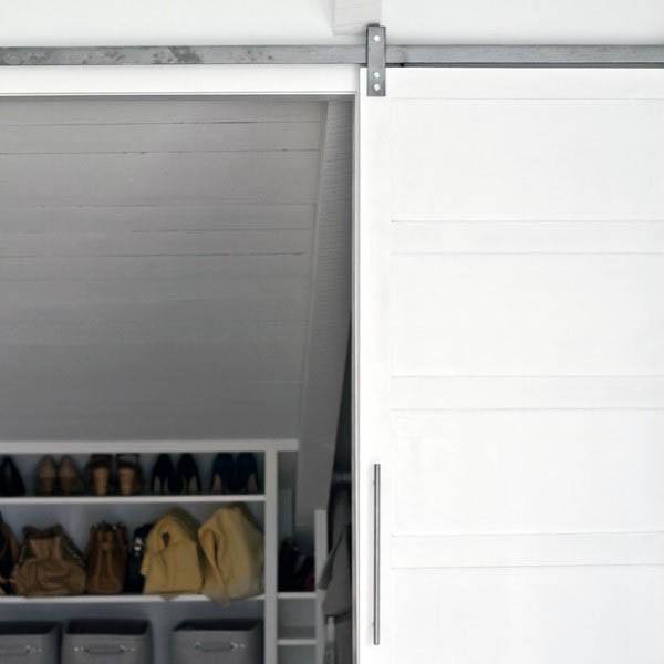 A white sliding door partially open, unveiling a closet with shelves for shoes, bags, and storage bins
