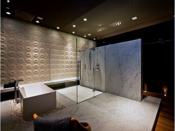 Modern bathroom with glass shower enclosure, white bathtub, and textured wall under soft lighting
