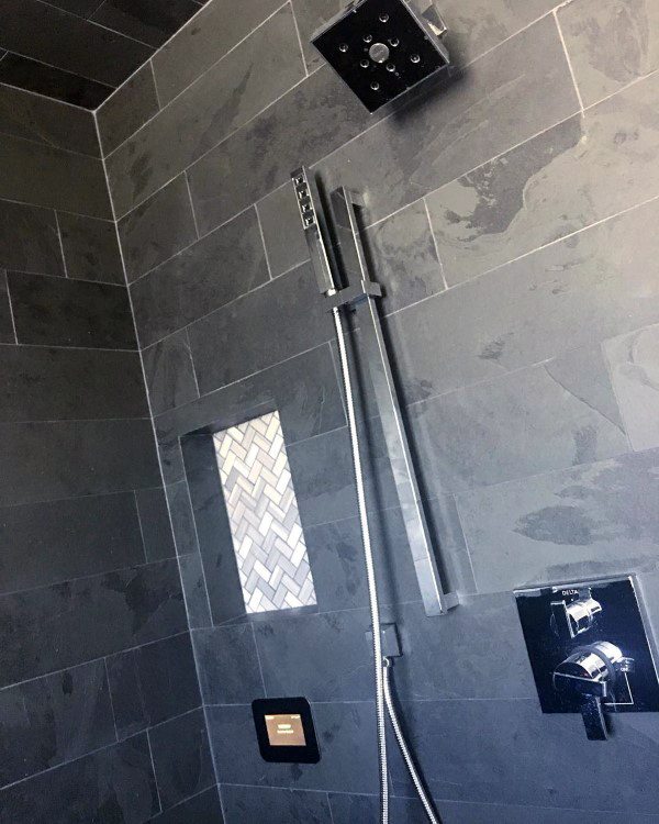 Modern shower with dark slate tiles, rainfall showerhead, and herringbone recessed shelf.