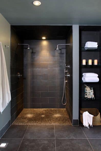 Modern shower room with dark tiles, dual showerheads, and shelving with towels