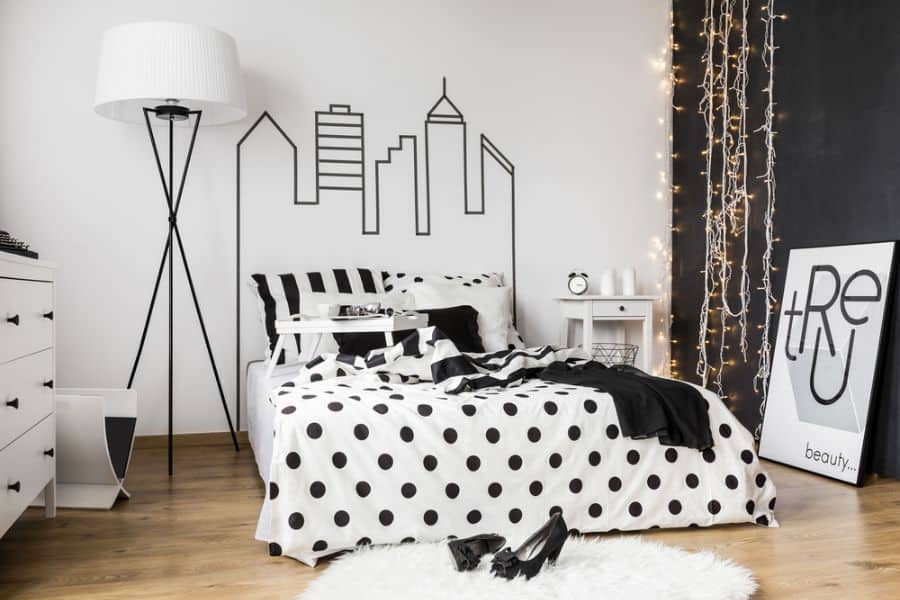 Modern bedroom with black and white decor, geometric bedding, framed art, and fairy lights.