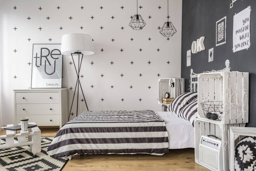 Stylish black and white bedroom with striped bedding, wooden crates as storage, pendant lights, and patterned walls.