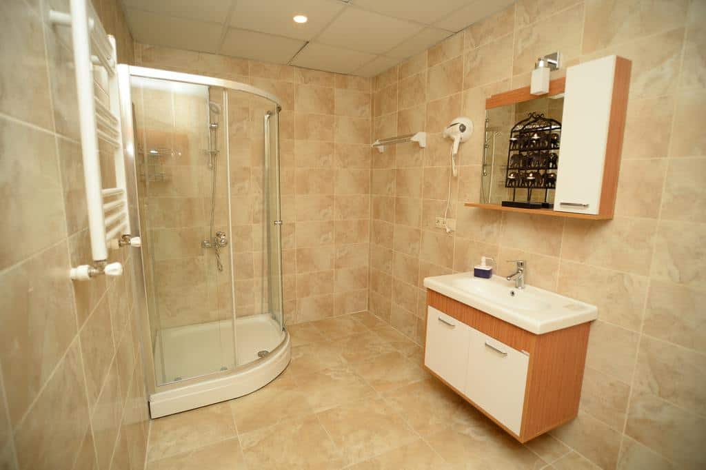 Modern bathroom with cream-colored tiles, corner shower, and wall-mounted vanity.