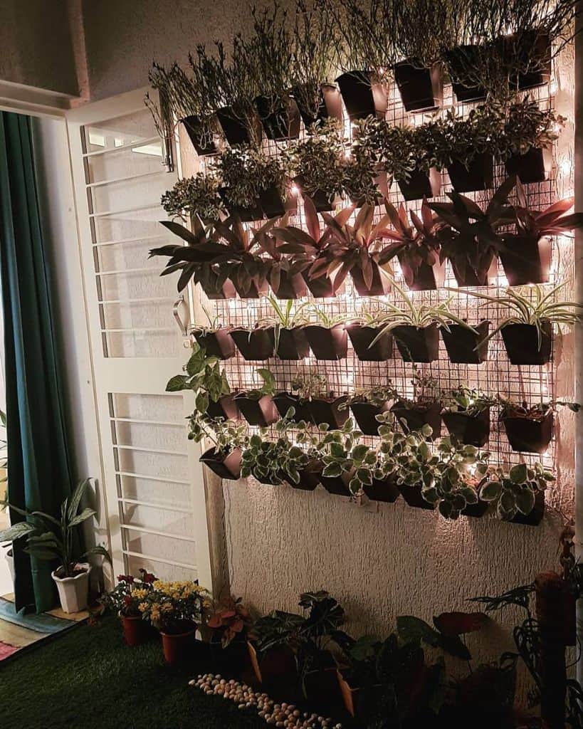 Illuminated vertical wall garden with potted plants and string lights on a small balcony.