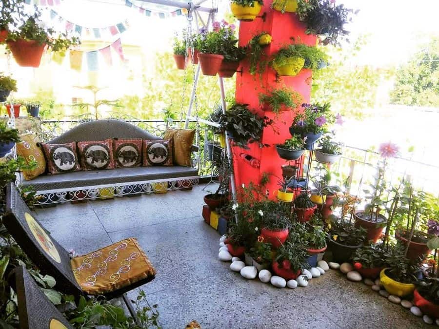 Colorful balcony garden with hanging planters, potted plants, and a cushioned swing.