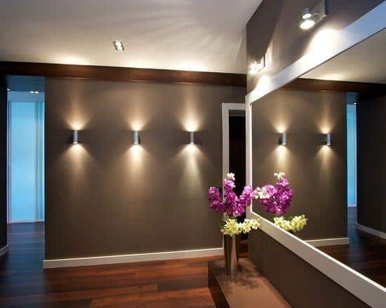Modern hallway with dark walls, decorative wall sconces, and large mirror with spotlight.