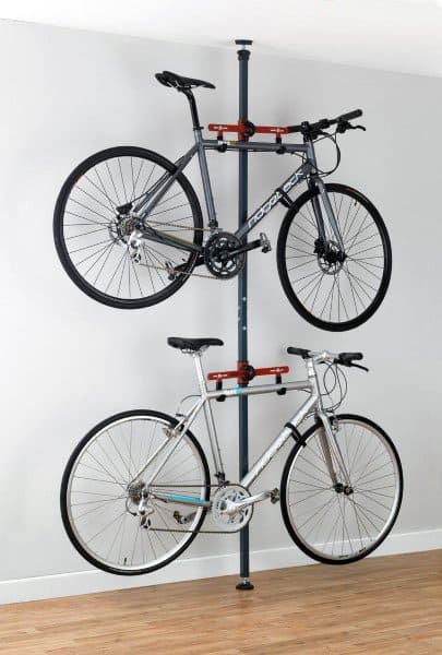 Two bikes stored on a vertical tension pole rack against a white wall in a clean room.