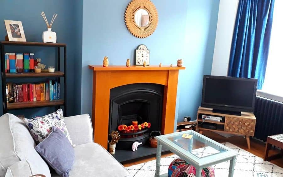 Eclectic living room with blue walls, orange fireplace, and cozy bookshelf decor.