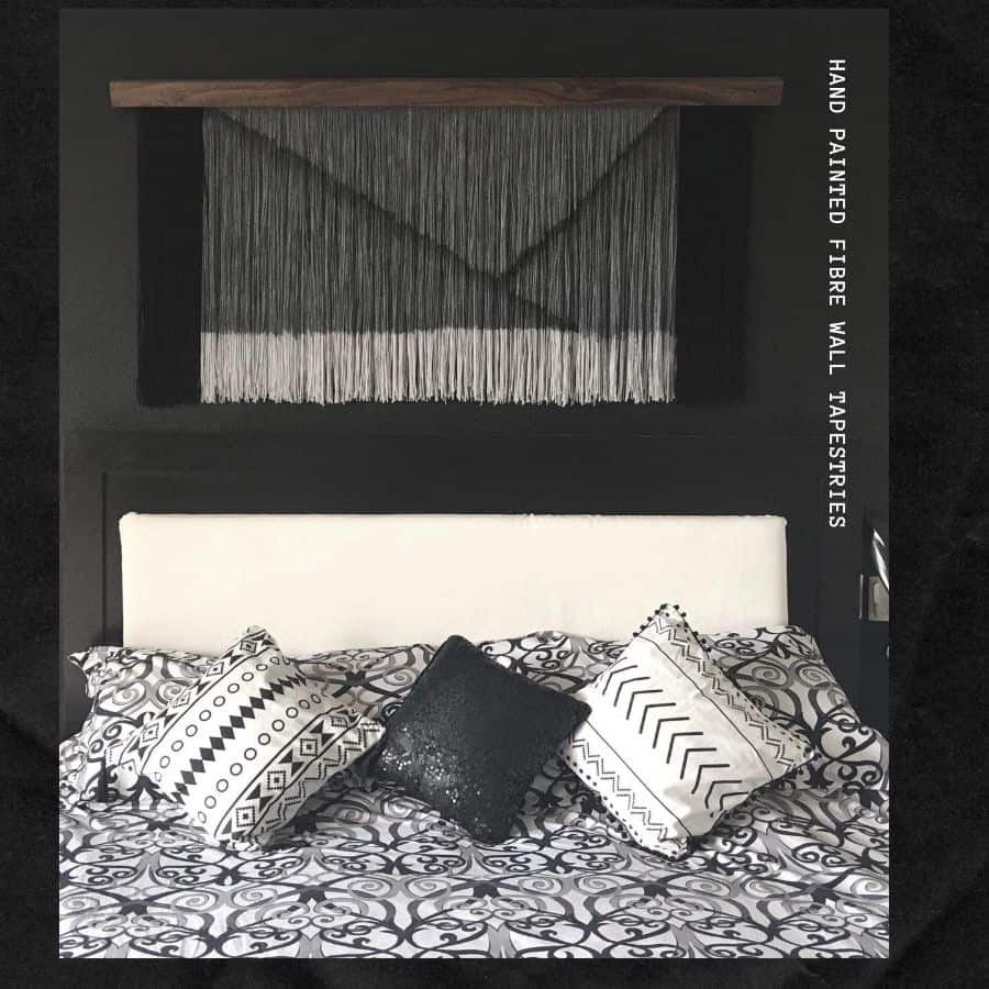 Black and white bedroom with abstract wall tapestry and patterned pillows.