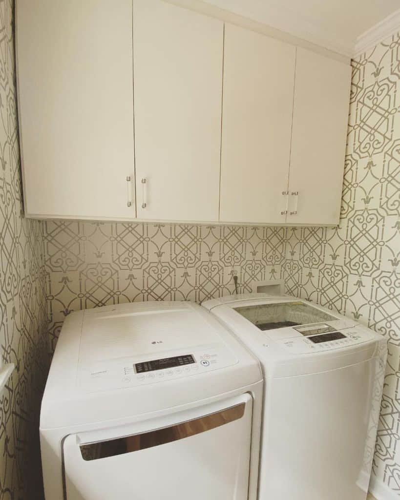 simple laundry with pattern wallpaper white cabinets and washer and dryer 