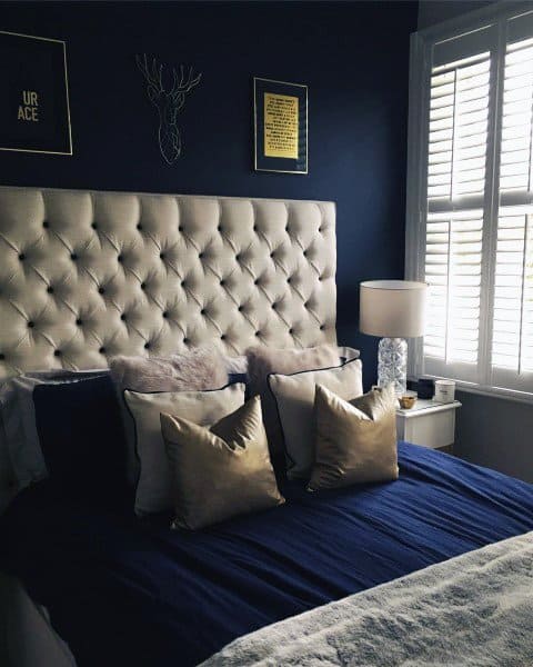Luxurious navy bedroom featuring a tufted headboard, cozy gold-accented pillows, and soft ambient lighting.