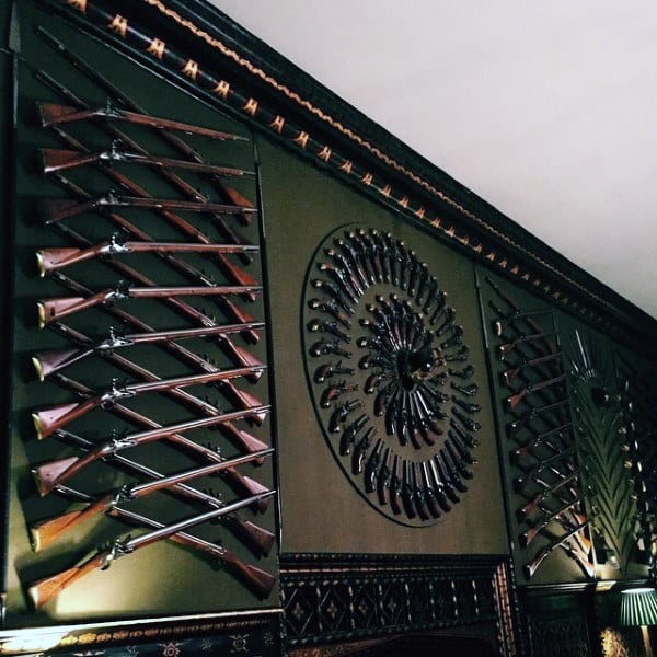 Artistic display of rifles and pistols on a green accent wall in a gun room.