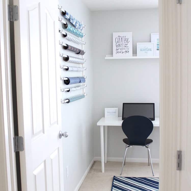 Minimal home office with a computer, a sleek black chair, and gift wrap rolls on the wall