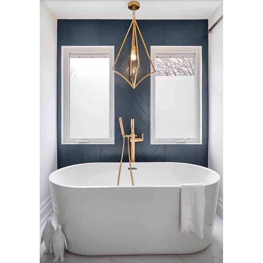Modern bathroom with a white freestanding tub, gold fixtures, a geometric pendant light, and dark accent wall