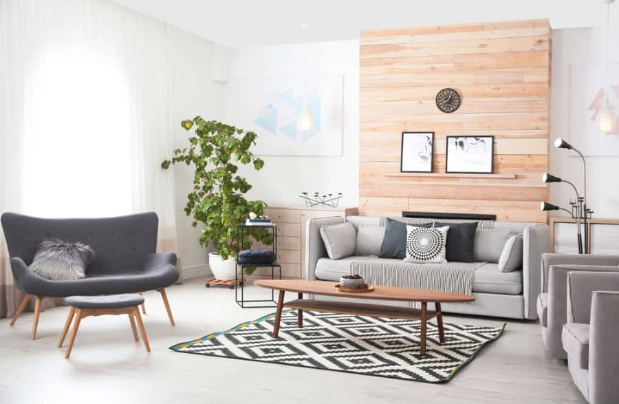 Modern living room with a gray sofa, chair, and a wooden coffee table on a geometric rug; natural light fills the space