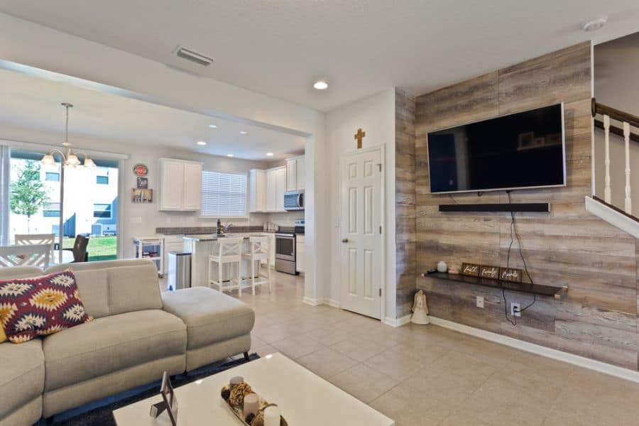 Modern living room with wall-mounted TV, sectional sofa, and open kitchen