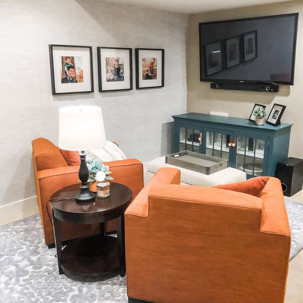 Cozy small living room with orange armchairs, wall-mounted TV, and framed photos.