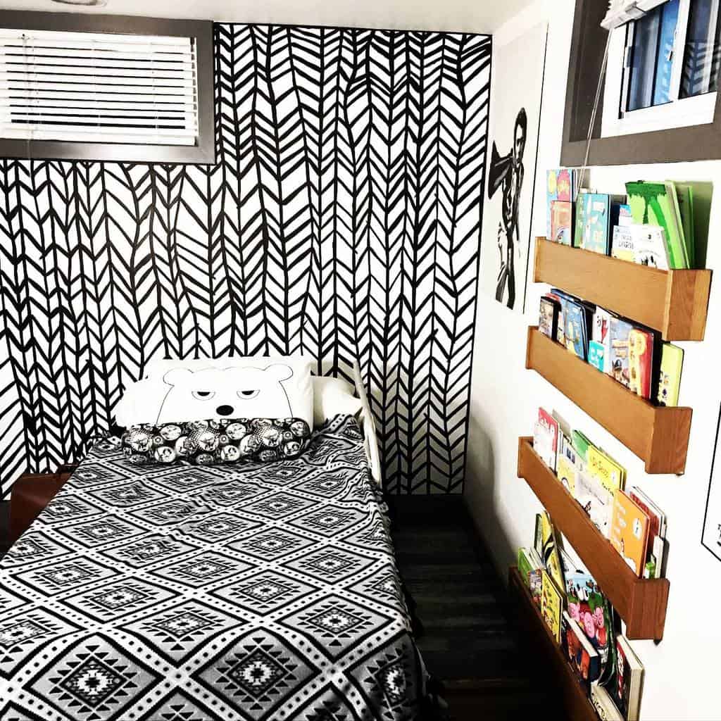 Kid's bedroom with black and white geometric wallpaper, bookshelf, and cozy bedding.