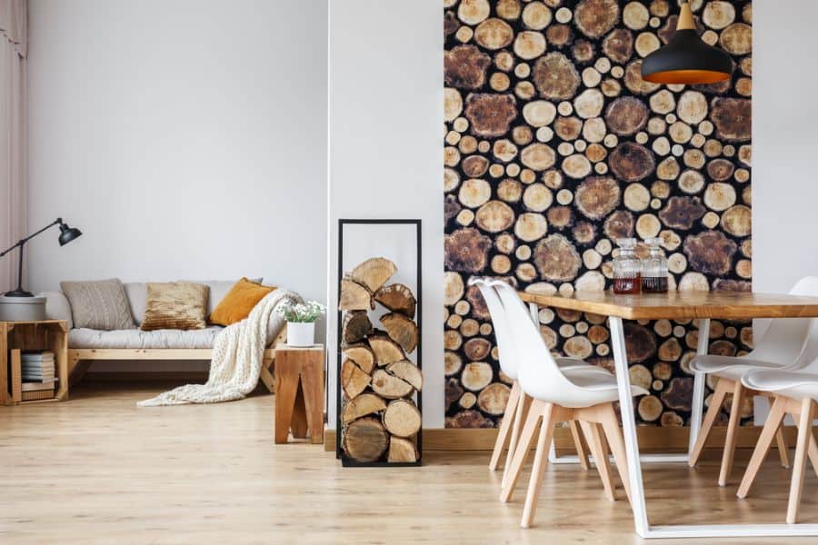 Modern living room with wood-themed decor, white chairs, wooden table, sofa, and a stacked log wall design