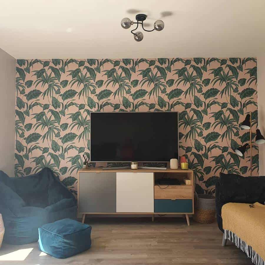 Living room with palm leaf wallpaper, TV on a console, teal bean bag chairs, and a black ceiling light fixture