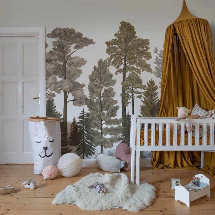 A cozy nursery with a forest mural, white crib with mustard canopy, and soft toys scattered on wooden floor